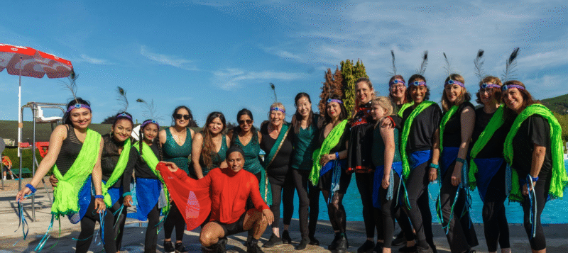 17 people standing in aline in colourful indian dance costumes